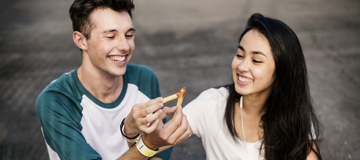 Zwei junge Menschen lachen miteinander während sie Pommes essen
