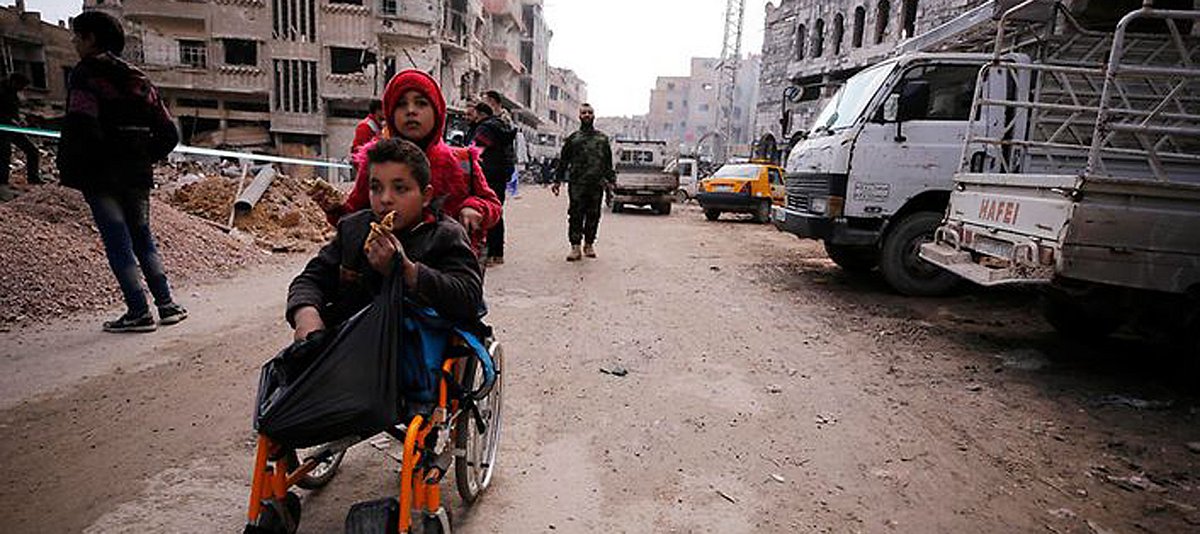 Ein Mädchen schiebt in der syrischen Stadt Douma einen Jungen im Rollstuhl, der seine Beine verloren hat.