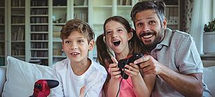 Ein Erwachsener und zwei Kinder spielen mit Controllern in der Hand