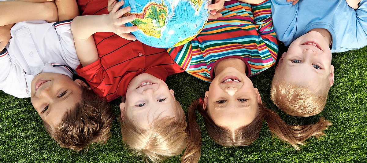 Vier Kinder liegen im Gras und halten in der Hand einen Globus.
