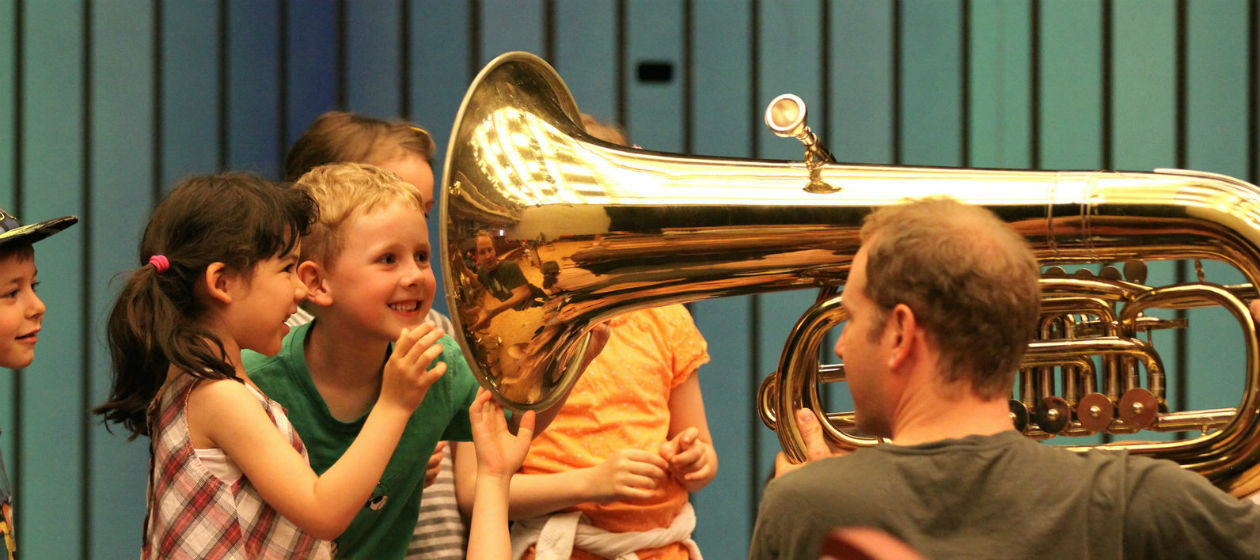 Kinder schauen neugierig in eine Tuba