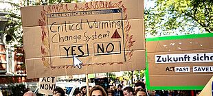 Ein Protestzug junger Menschen, im Zentrum ein Schild mit der Aufschrift Critical Warming - Change System? und einem Pfeil, der auf Yes deutet