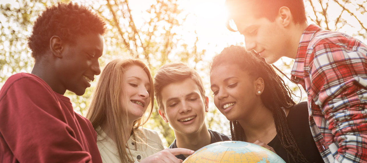 Jugendliche unterschiedlicher Herkunft halten einen Globus und lächeln dabei.