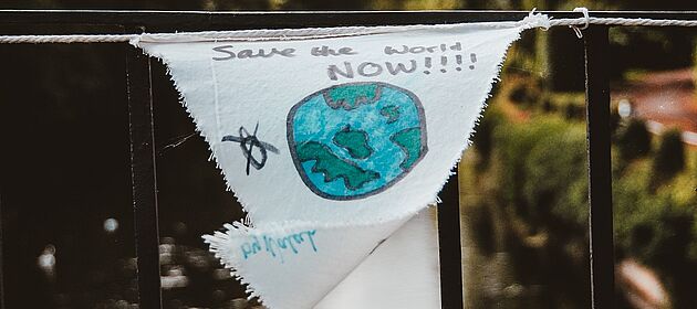 Ein Stück Stoff auf dem eine Erdkugel gemalt ist, über der Save the World Now! steht