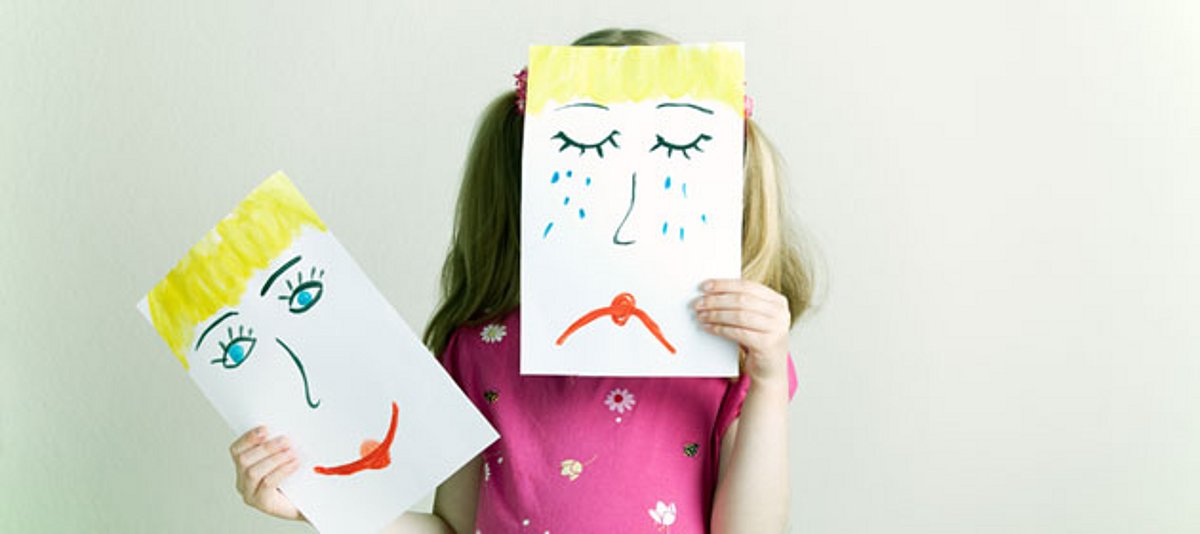 Ein Mädchen hält ein gemaltes trauriges Gesicht vor ihr Gesicht.