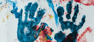 Auf einem Papier sind Abdrücke von Kinderhänden in blauer Farbe zu sehen