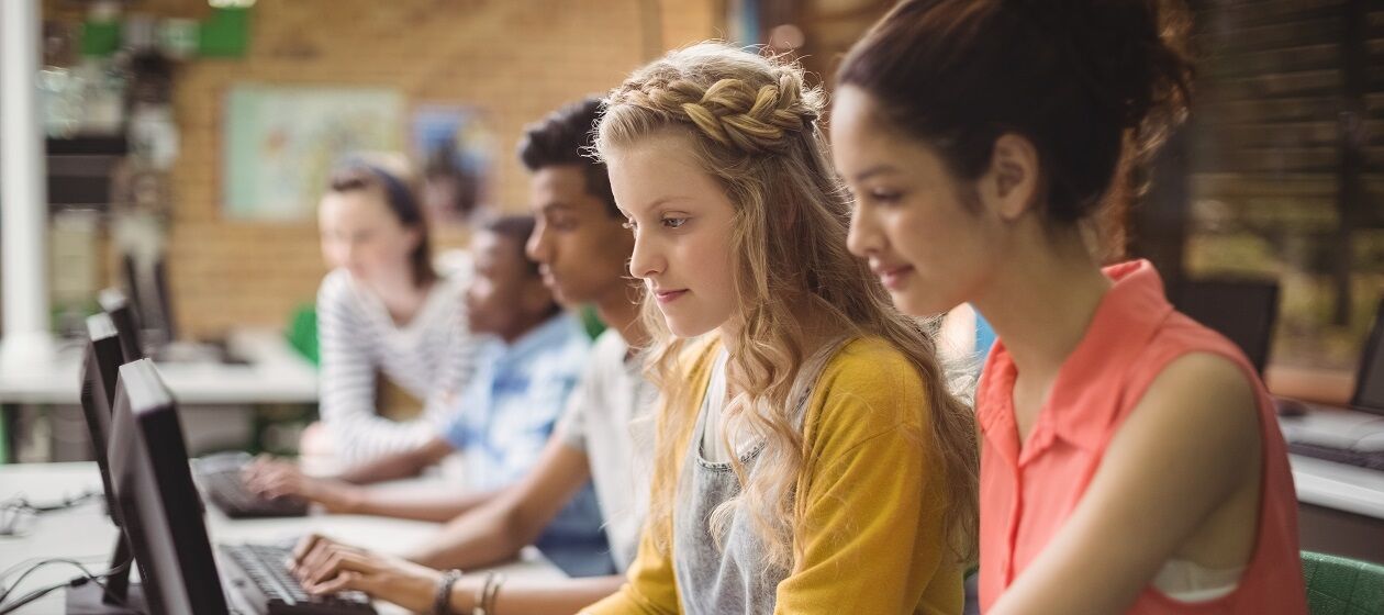Mehrere Jugendliche sitzen in einem Klassenzimmer an Laptops