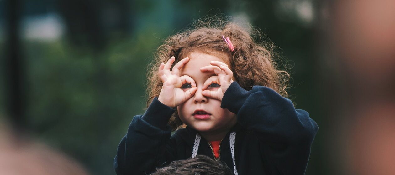Ein Mädchen formt mit seinen Fingern eine Brille und schaut hindurch