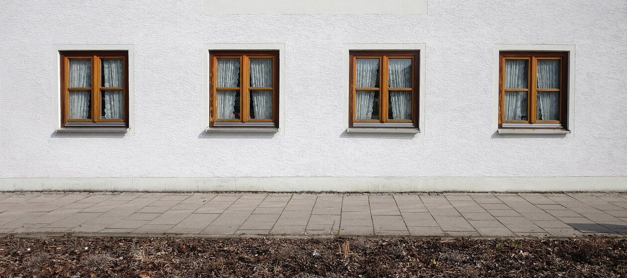 Eine Häuserfront mit vier gleichen Fenstern mit zugezogenen Vorhängen