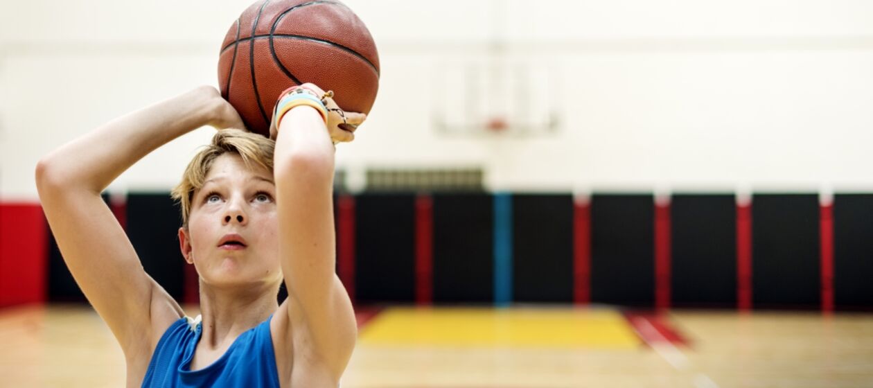 Ein Junge spielt in einer Turnhalle Basketball