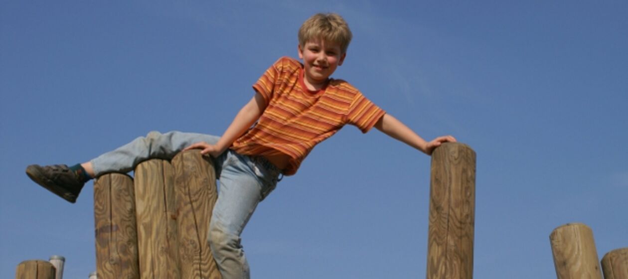 Ein Junge turnt auf Holzbalken.