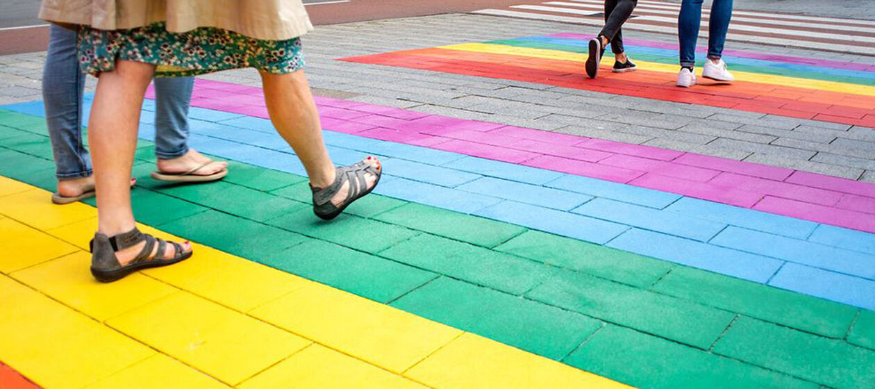 Mehrere Menschen laufen in Sandalen und Turnschuhen über einen in bunten Farben bemalten Fußboden. 