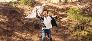 Ein Kind hat einen selbstgebauten Drachen in der Hand und läuft durch den Wald