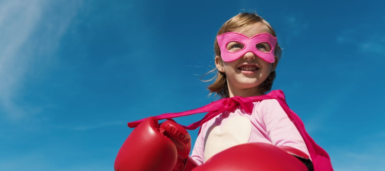 Mädchen mit rosa Maske und roten Boxhandschuhen steht vor blauem Himmel