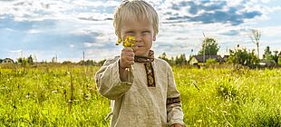 Ein Kind steht auf einer Wiese und hält Blumen in der Hand