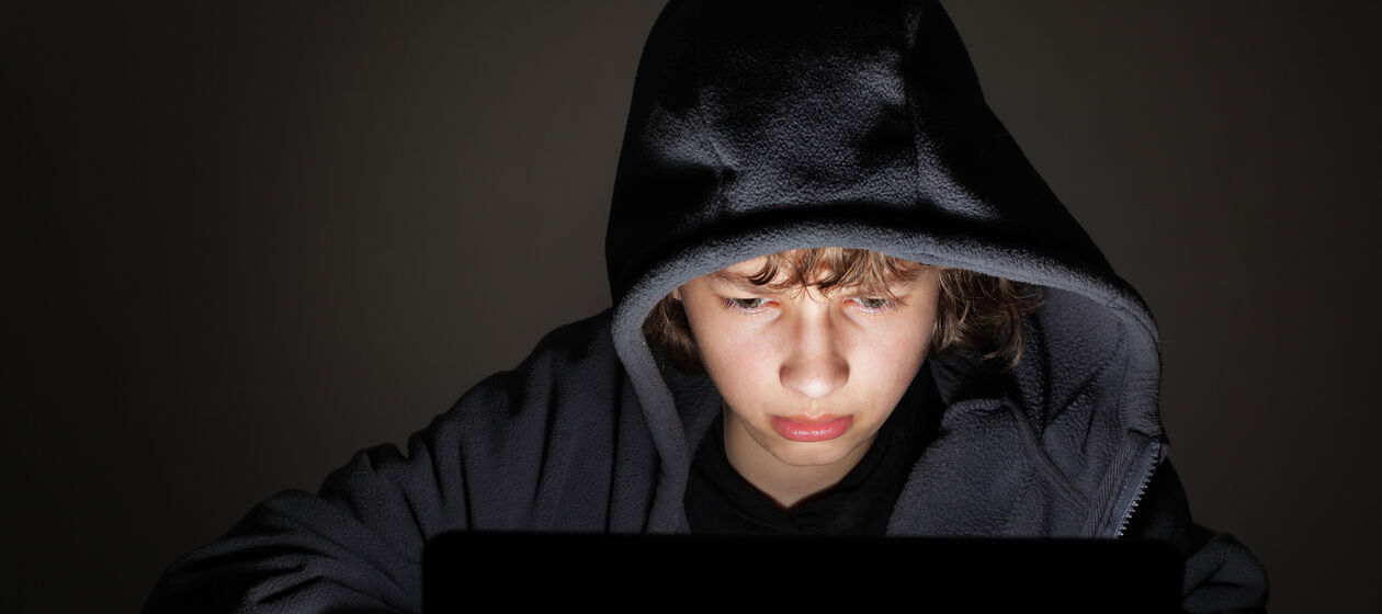 Jugendlicher mit Kapuze vor Computer