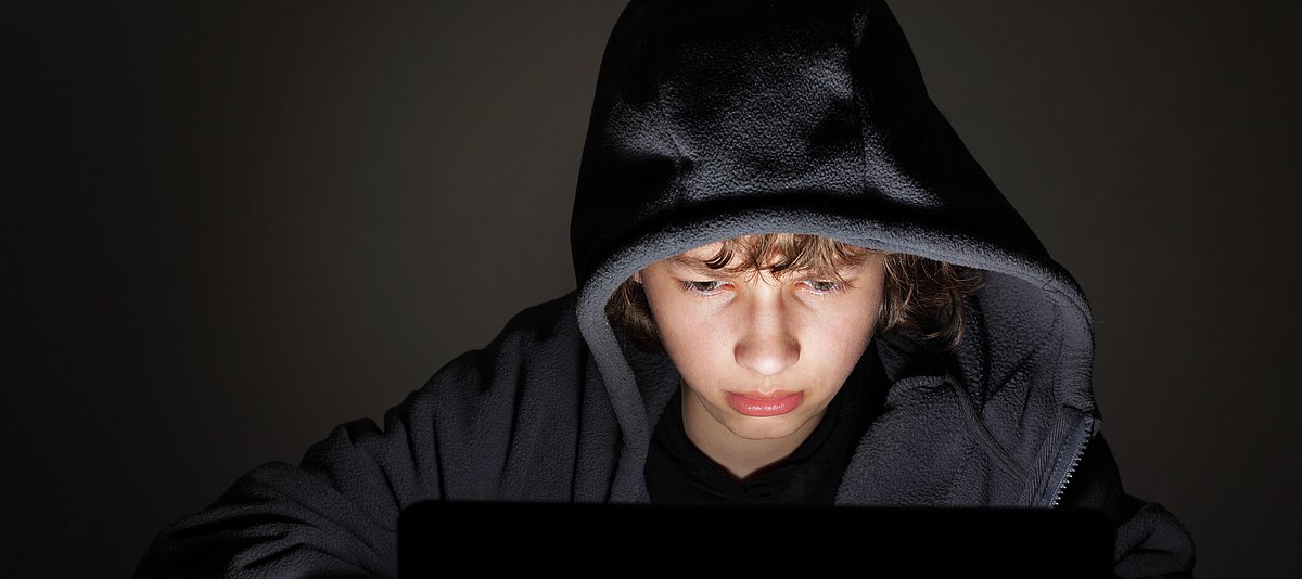 Jugendlicher mit Kapuze vor Computer