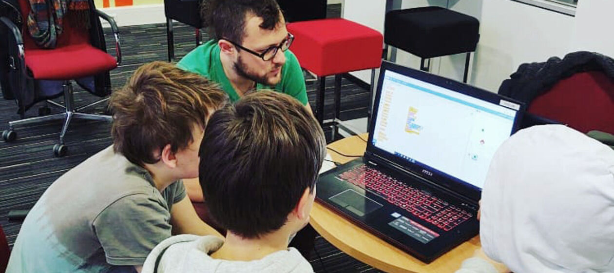 Zusammen mit einem Medienpädagogen sitzen drei Jugendliche um einen Computer.