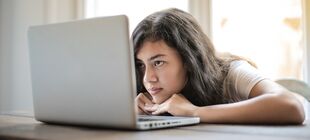 Jugendliche sitzt vor einem Laptop und hat das Kinn auf die Hände gestützt