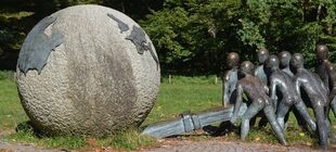 Kupfer-Beton-Skulptur im Park: Eine Gruppe Männer hebelt eine Weltkugel an.