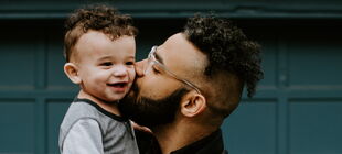 Ein Vater hält seinen kleinen Sohn auf dem Arm und küsst ihn auf die Wange