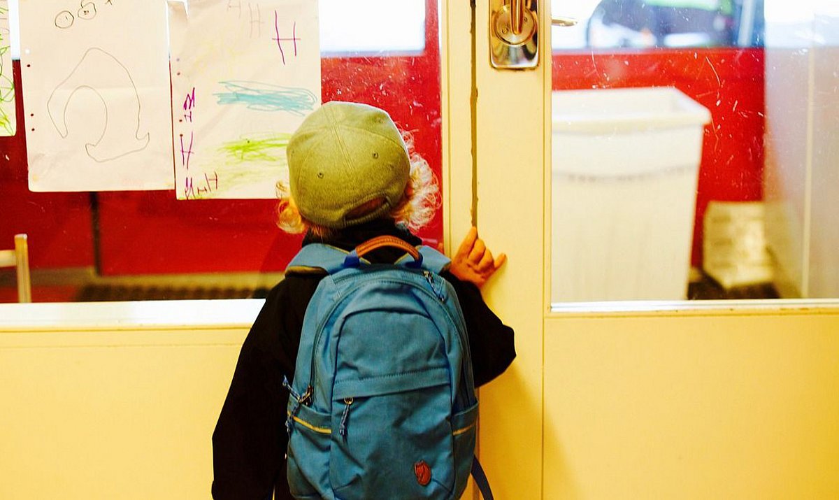 Ein kleiner Junge steht an einer Tür am Eingang in die Kita