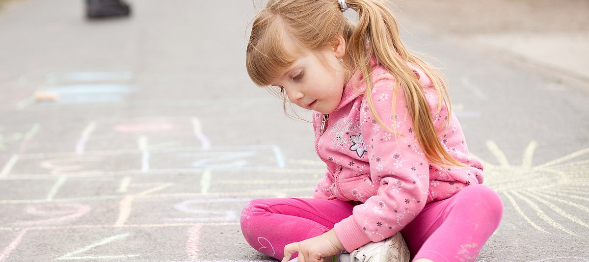 Kind mit Kreide malt auf der Straße