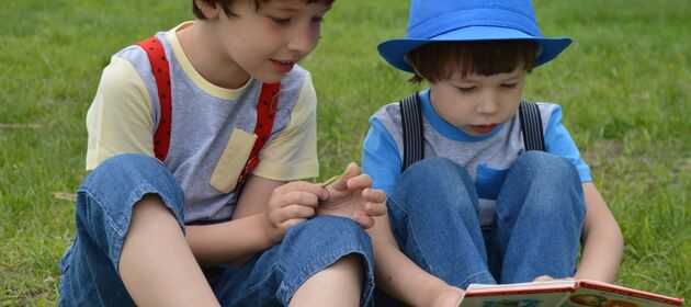 Zwei Jungen sitzen auf einer Wiese und schauen sich ein Buch an