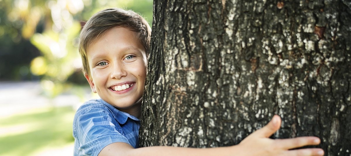 Ein vor Freude strahlender Junge umarmt einen Baumstamm