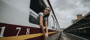Eine junge Frau lehnt sich aus einem Zugfenster und schaut in einen leeren Bahnhof