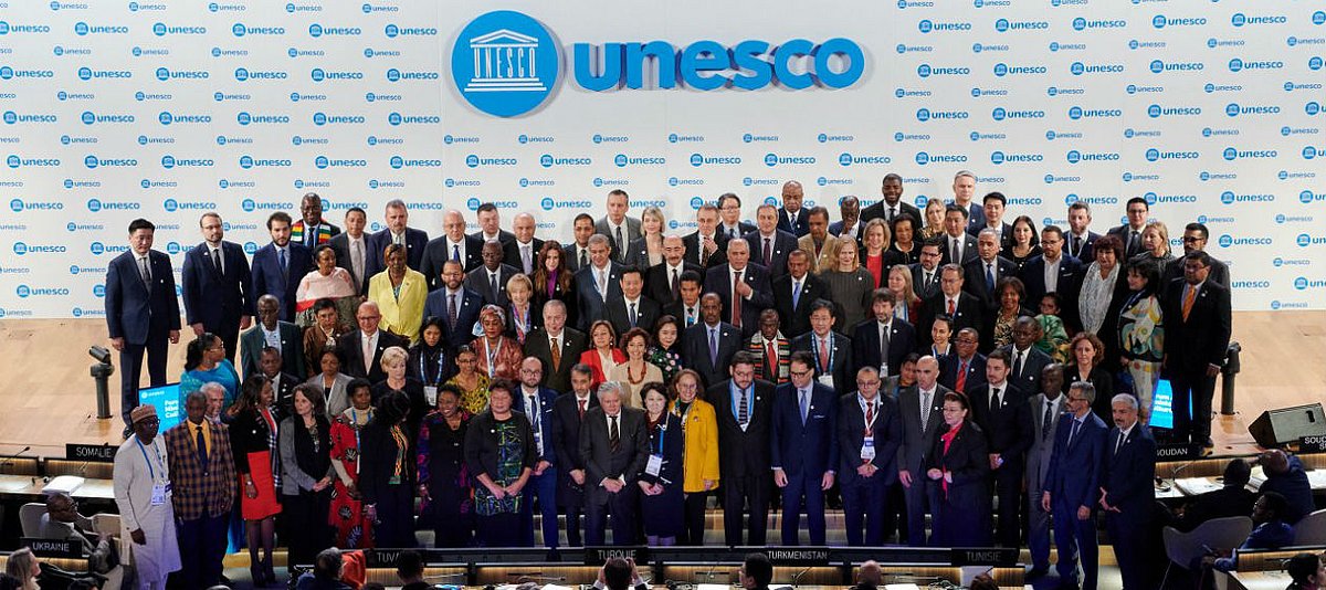 Vor dem Schriftzug "UNESCO" steht eine Gruppe von Männern und Frauen