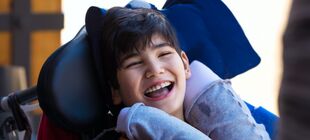 Kind mit Beeinträchtigung im Rollstuhl lacht in die Kamera