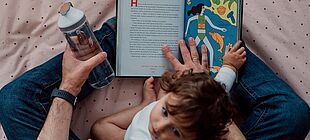 Eine erwachsene Person liest einem Kleinkind aus einem Buch vor