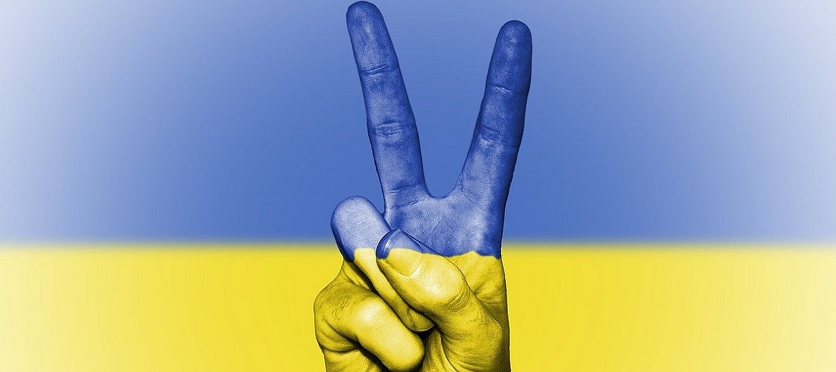 Peace-Handzeichen vor einem blau-gelben Hintergrund