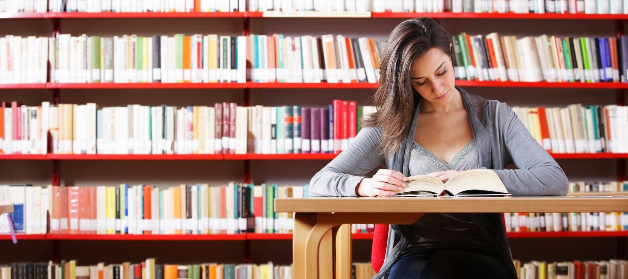 Eine junge Frau sitzt in der Uni-Bibliothek und liest