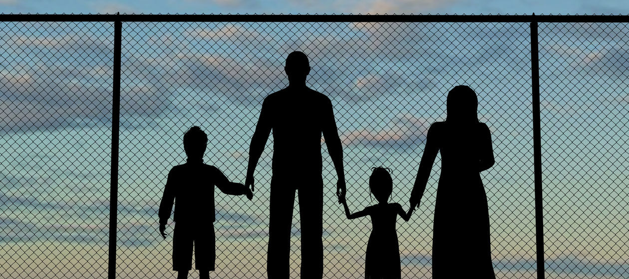 Eine Familie ist als Silhouette an einem Zaun stehend zu sehen.