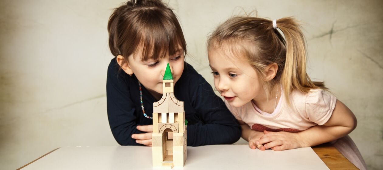 Zwei Kinder bestaunen einen Turm aus Holzklötzen