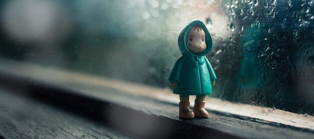 Eine Holffigur, die ein trauriges Kind darstellt, steht vor einer Fensterscheibe mit Regentropfen 