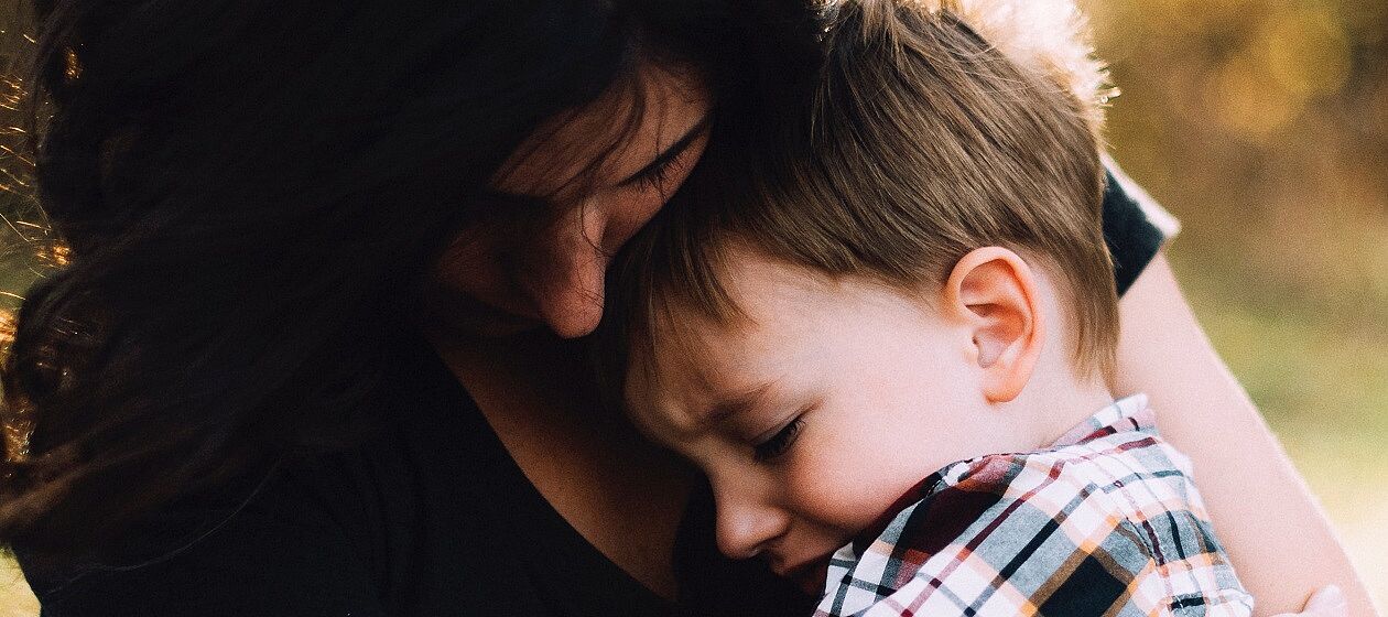 Eine Frau tröstet einen traurigen kleinen Jungen und hält ihn im Arm.
