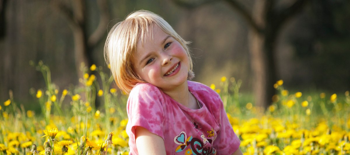 Ein Kind sitzt in einer Blumenwiese und lächelt
