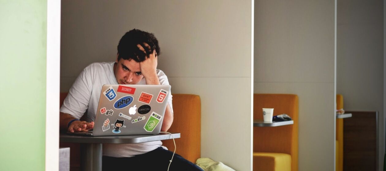 Junger Mann schaut auf seinen Laptop und stützt seinen Kopf auf