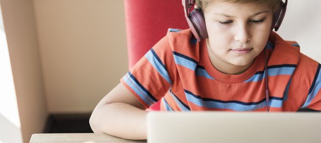 Eine Junge sitzt mit Kopfhörern vor einem Laptop und schaut auf den Bildschirm