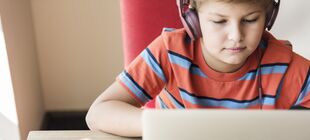 Eine Junge sitzt mit Kopfhörern vor einem Laptop und schaut auf den Bildschirm