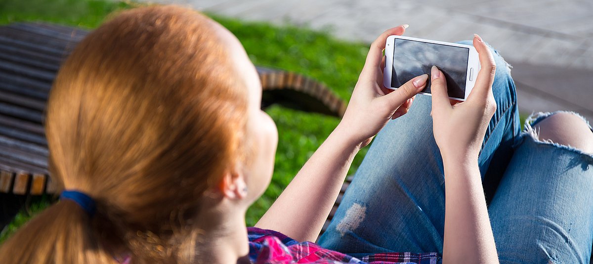 Mädchen sitzt im Gras mit Smartphone