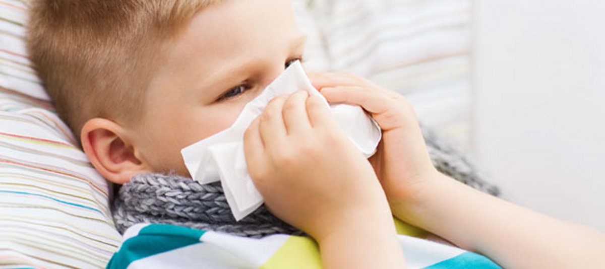 Ein Junge liegt krank im Bett und putzt sich die Nase