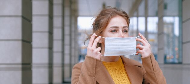 Eine junge Frau setzt ihre Mund-Nase-Bedeckung auf