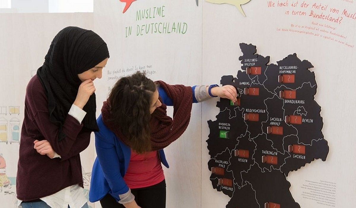 Zwei Schülerinnen, davon eine mit Kopftuch, stehen vor einer interaktiven Deutschlandkarte in der Ausstellung "Muslime in Deutschland".
