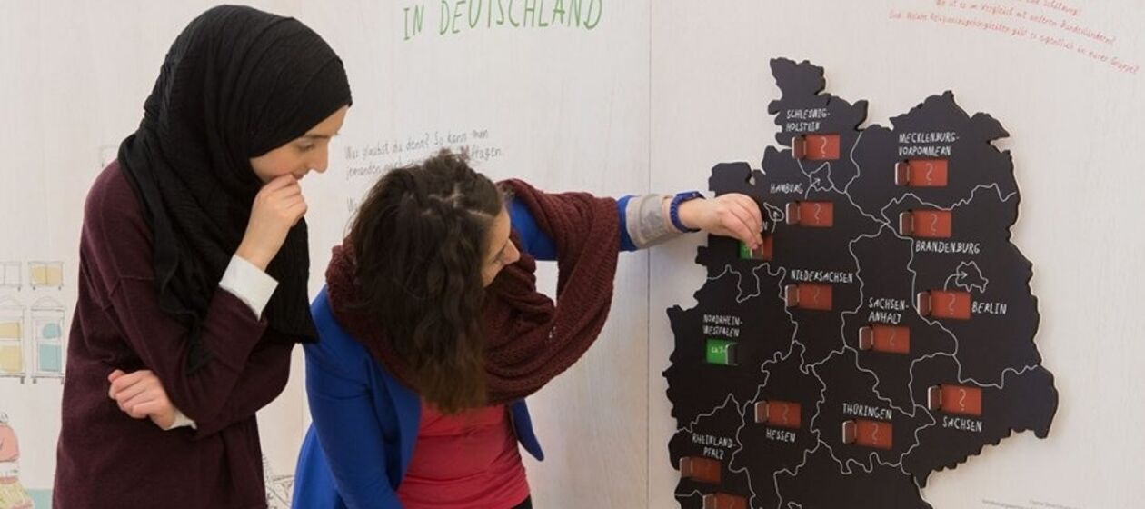 Zwei Schülerinnen, davon eine mit Kopftuch, stehen vor einer interaktiven Deutschlandkarte in der Ausstellung "Muslime in Deutschland".
