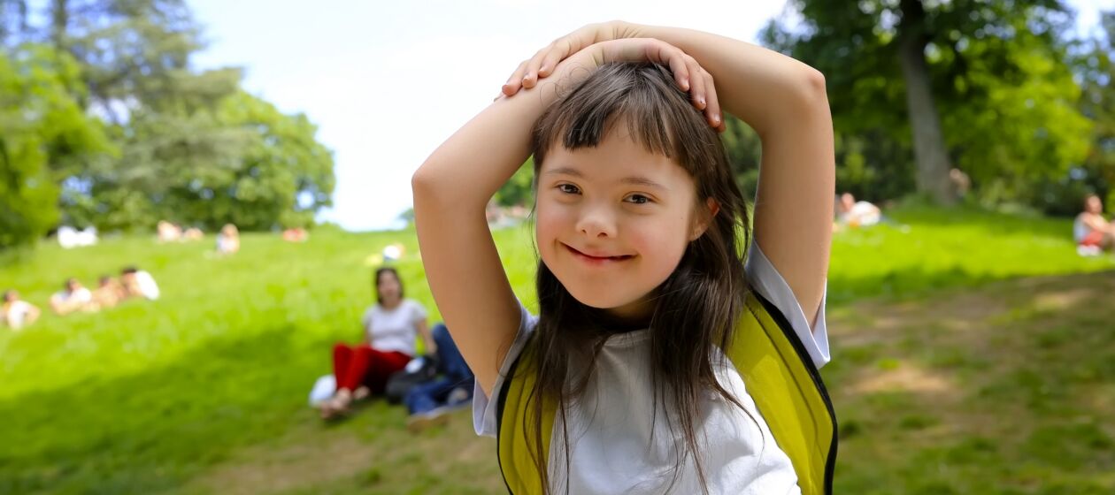 Mädchen mit Down-Syndrom auf einer Wiese im Park lächelt glücklich 