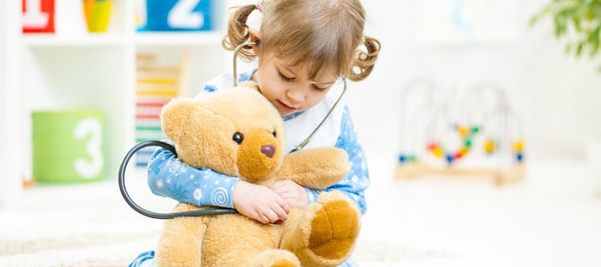 Ein kleines Mädchen untersucht seinen Teddy mit einem Stethoskop